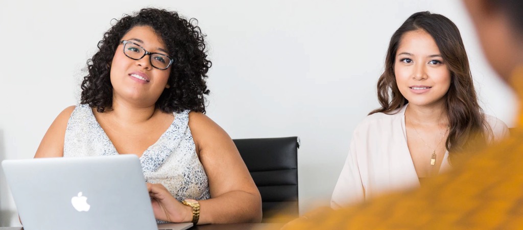 Two women interviewing someone we can bearly see in the forground
